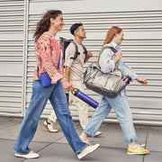 Three people walking outdoors with bags, wearing casual clothing.