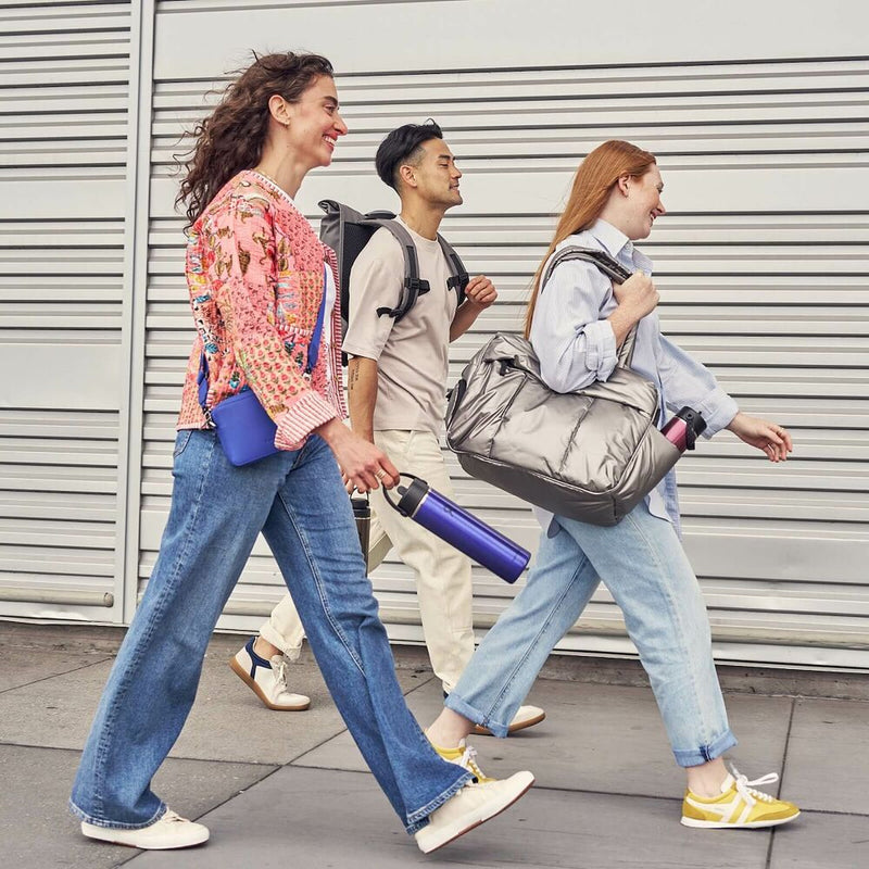 Three people walking outdoors with bags, wearing casual clothing.