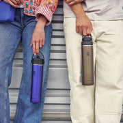 Two people holding insulated water bottles against a striped background