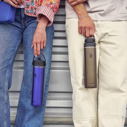 Two people holding insulated water bottles against a striped background