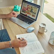 Person using a laptop with a notebook and mug on a desk