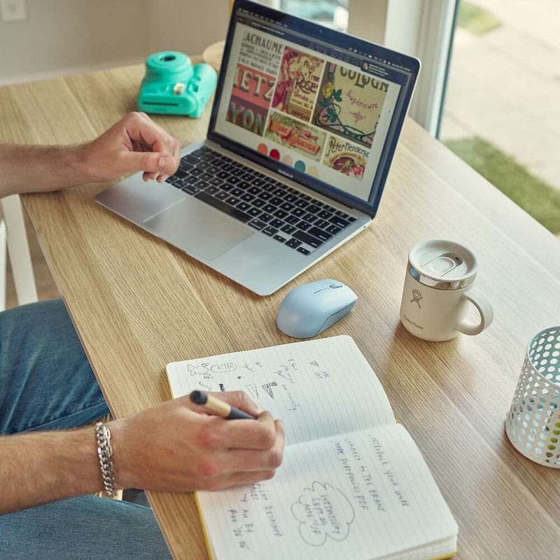 Person using a laptop with a notebook and mug on a desk