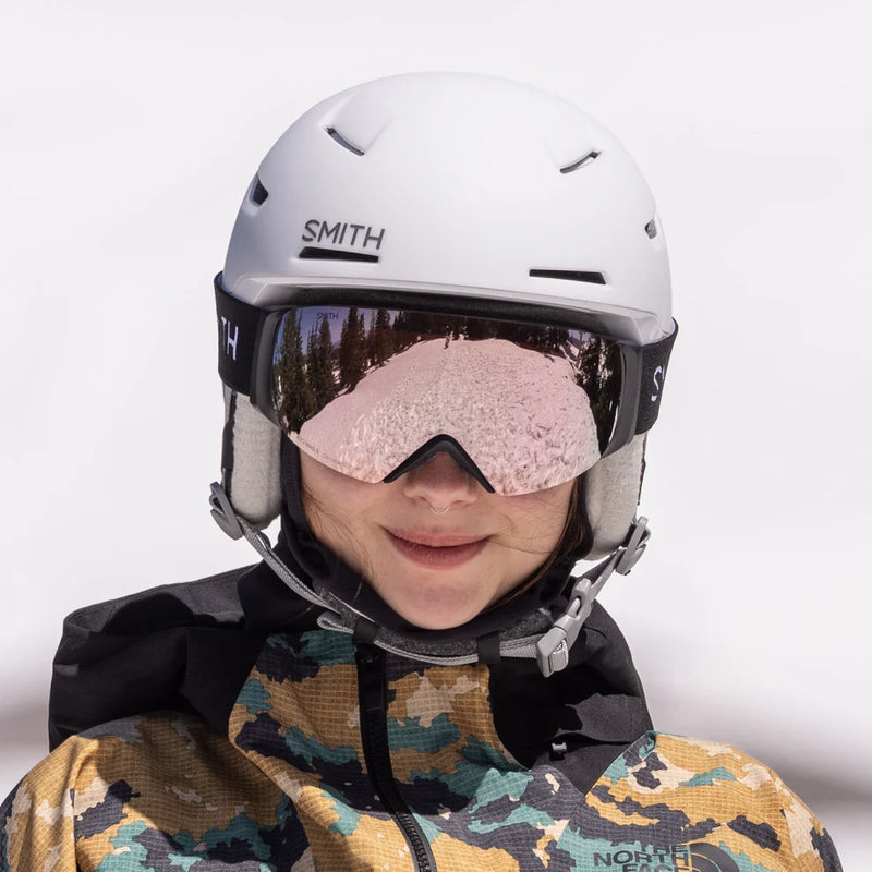 Person wearing a white Smith helmet and goggles with a camouflage jacket on a white background