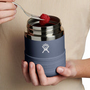Person holding a Hydro Flask insulated food jar with a raspberry on top, against a beige background.