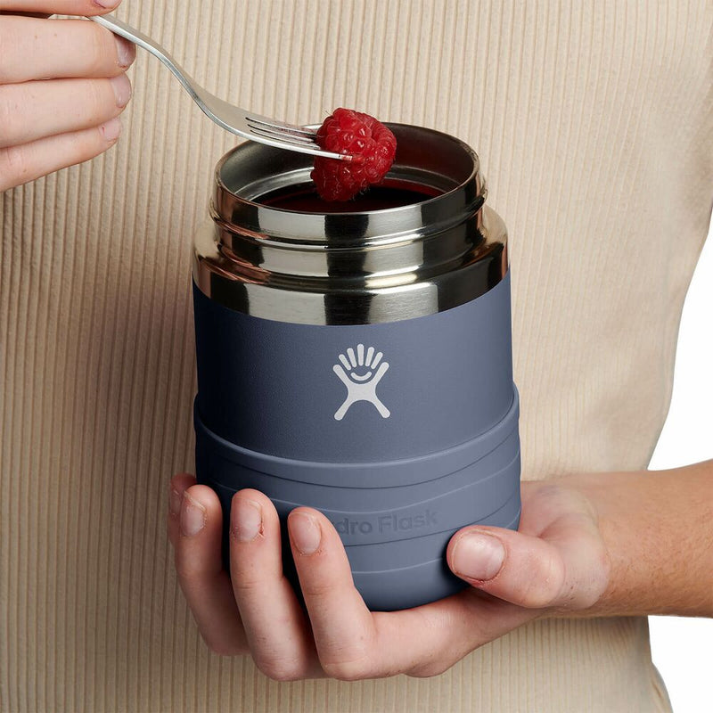 Person holding a Hydro Flask insulated food jar with a raspberry on top, against a beige background.