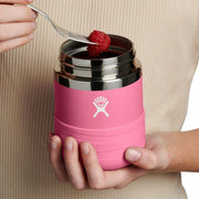 Pink thermos with silver lid held by a person, containing a raspberry.