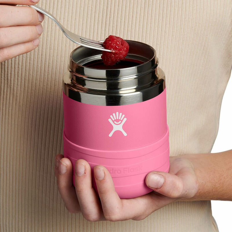 Pink thermos with silver lid held by a person, containing a raspberry.