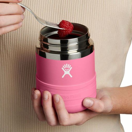 Pink thermos with silver lid held by a person, containing a raspberry.