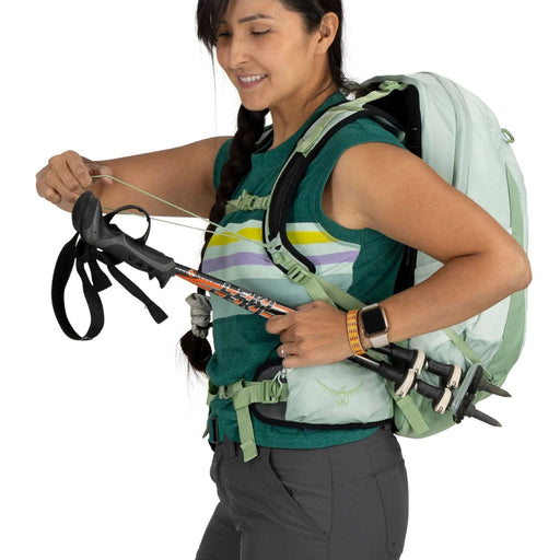 Person wearing a green top and carrying a backpack with hiking equipment on a white background