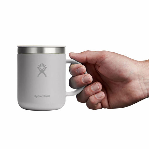 Hand holding up a silvery grey Hydro Flask mug with matching lid