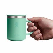 A mint green Hydro Flask insulated mug with a stainless steel rim, held by a hand against a solid white background.