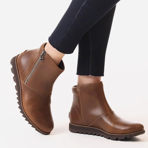 Brown ankle boots with zippers worn by a person on a white background