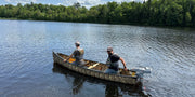 Two men in a camouflage patterned canoe floating in a lake. 