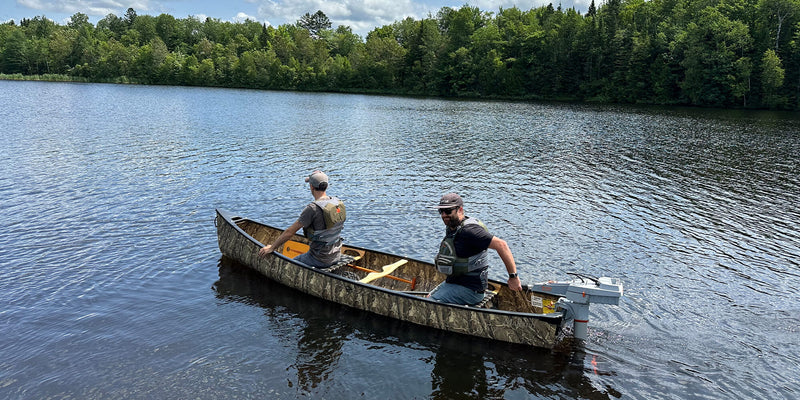 Two men in a camouflage patterned canoe floating in a lake. 