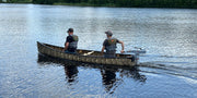 Two men in a camouflage patterned canoe floating on a lake. 