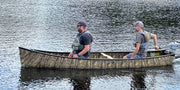 Two men in a camouflage patterned canoe floating on a lake. 