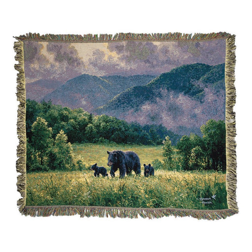 Throw blanket featuring a bear and her cubs walking through a meadow against a white background. 