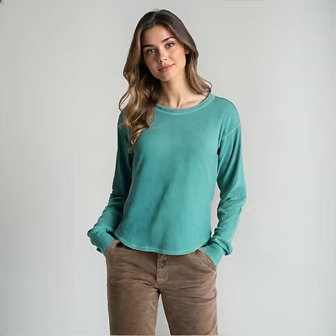 Woman wearing an arctic blue long sleeve shirt with her hands in her pockets against a grey background. 