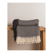 Black and white throw blanket with a wavy pattern sitting on a wooden shelf against a white wall. 