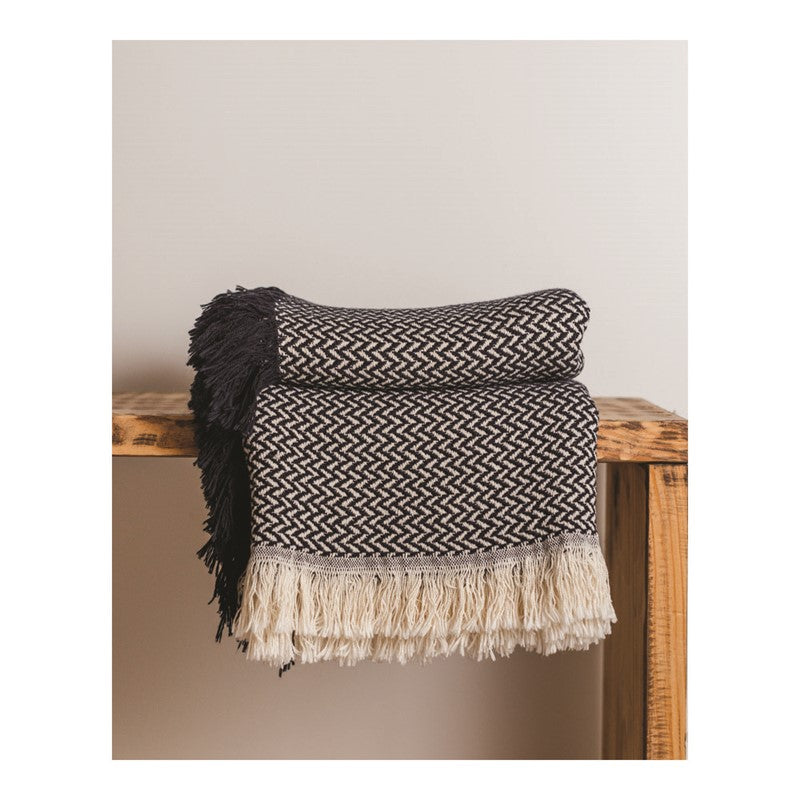 Black and white throw blanket with a wavy pattern sitting on a wooden shelf against a white wall. 