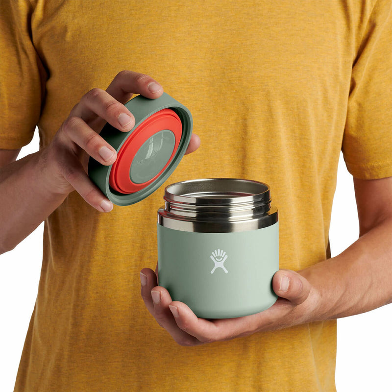 Person opening a sage green Hydro Flask food jar against a white background. 