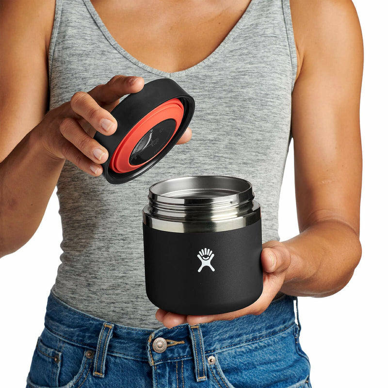 Person opening a black Hydro Flask food jar against a white background. 