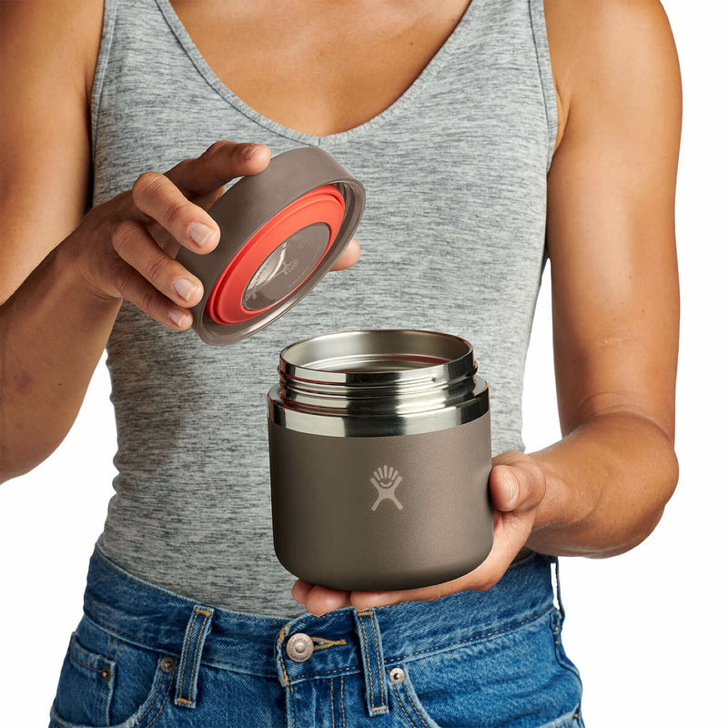 Person opening a brown Hydro Flask food jar against a white background. 