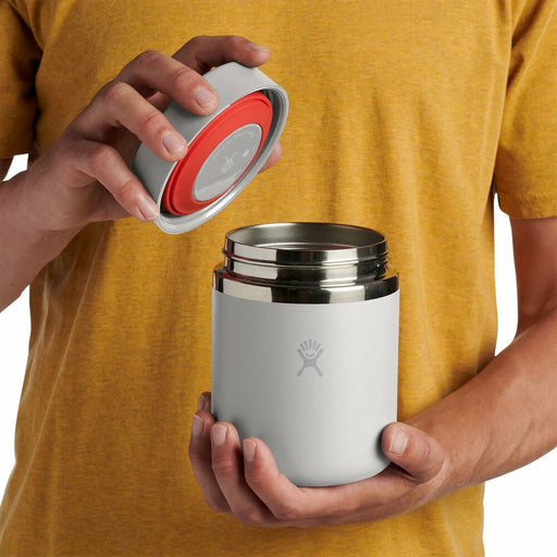 Person holding a white thermos with a red lid, wearing a yellow shirt.