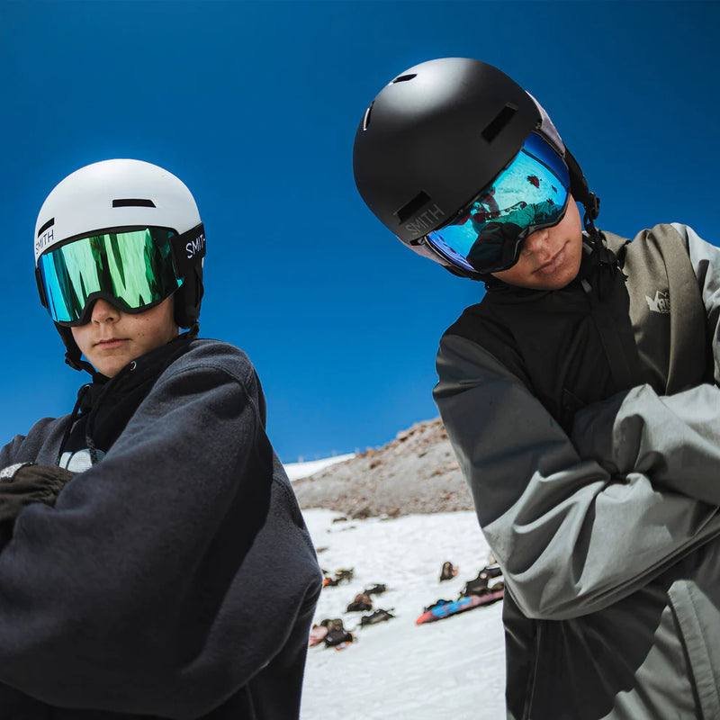 Two skiers in winter gear with goggles against a snowy mountain background