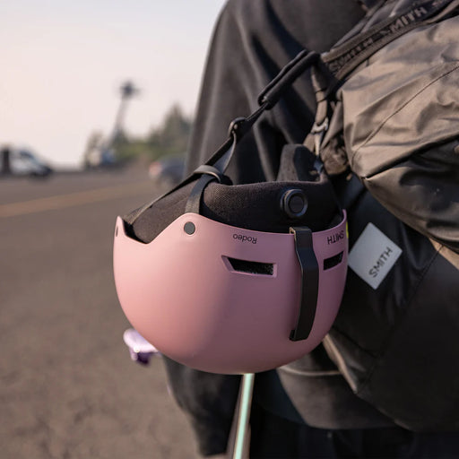 Pink helmet hanging from a backpack with a blurred street background