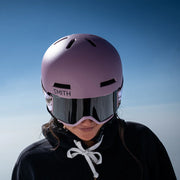 Person wearing a pink Smith helmet and goggles against a clear blue sky