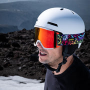 Person wearing a white helmet and goggles with colorful strap in a mountainous landscape