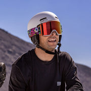 Person wearing a white helmet and colorful goggles with a mountainous background
