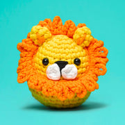 Crocheted lion toy with orange mane and yellow body on a teal background