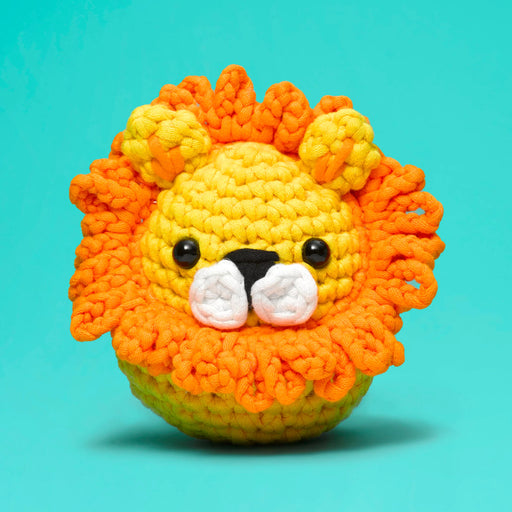 Crocheted lion toy with orange mane and yellow body on a teal background
