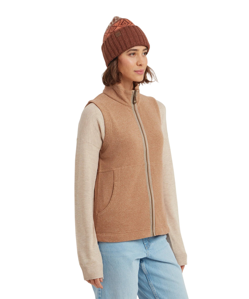 Woman wearing a brown vest, beige long-sleeve shirt, and blue jeans on a white background