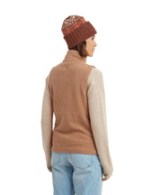 Person wearing a brown knit beanie, brown sweater, beige long-sleeve shirt, and light blue jeans on a white background