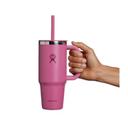 A pink Hydro Flask travel mug with a handle, lid, and straw, held by a person's hand against a plain white background.