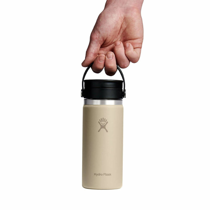 Hand holding a beige Hydro Flask bottle by the loop on the lid