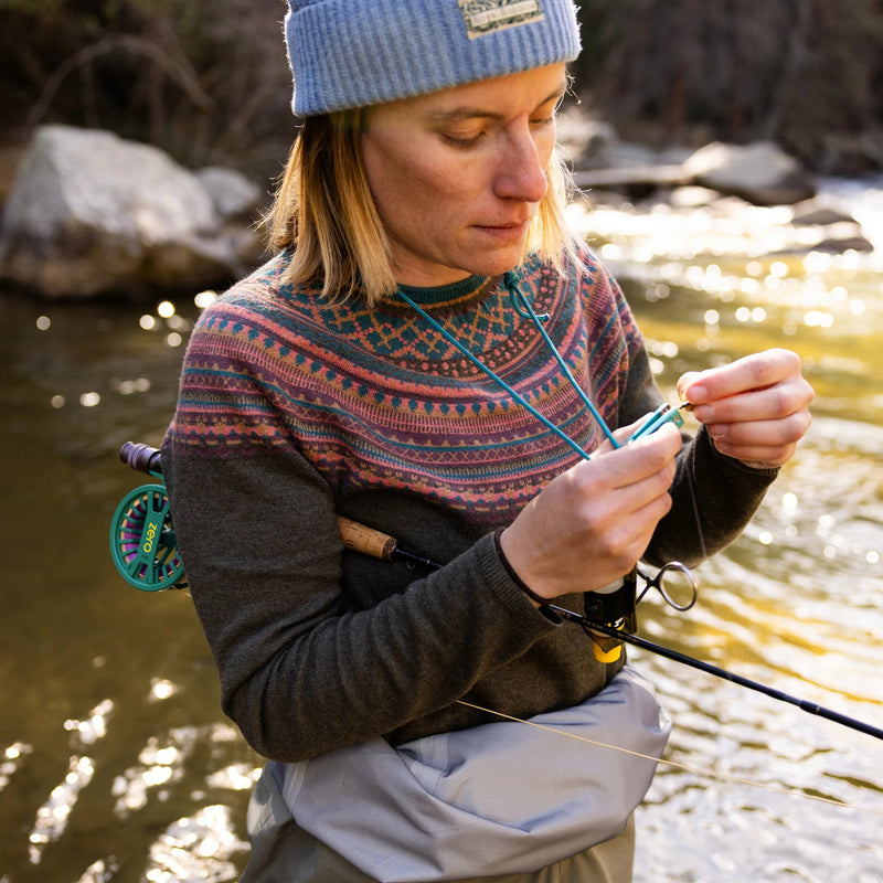 A person outside holding a fishing pole wearing a green sweater with a pink and blue pattern on the toptop